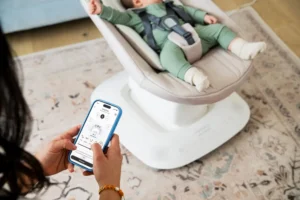 Neonato sdraiato in una sdraietta elettrica con controllo tramite smartphone in mano di un adulto