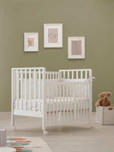 lettino bianco per bambini con sponde a listelli e ruote in una stanza con pareti verdi