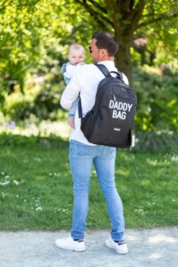 Uomo con zaino nero Daddy Bag che tiene in braccio un bambino in un parco