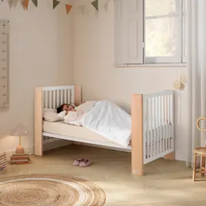 lettino per bambini con sponde bianche e angoli in legno chiaro con bambino sotto coperta bianca in una stanza luminosa
