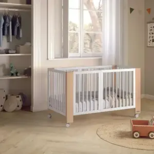 lettino per bambini con sponde bianche e angoli in legno chiaro su ruote in una stanza con pavimento in legno