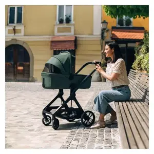 Donna seduta su una panchina che spinge un passeggino modulare con navicella in un'area urbana acciottolata