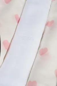 Tre mussole piegate con due a fantasia di cuori rosa e una bianca con logo ricamato